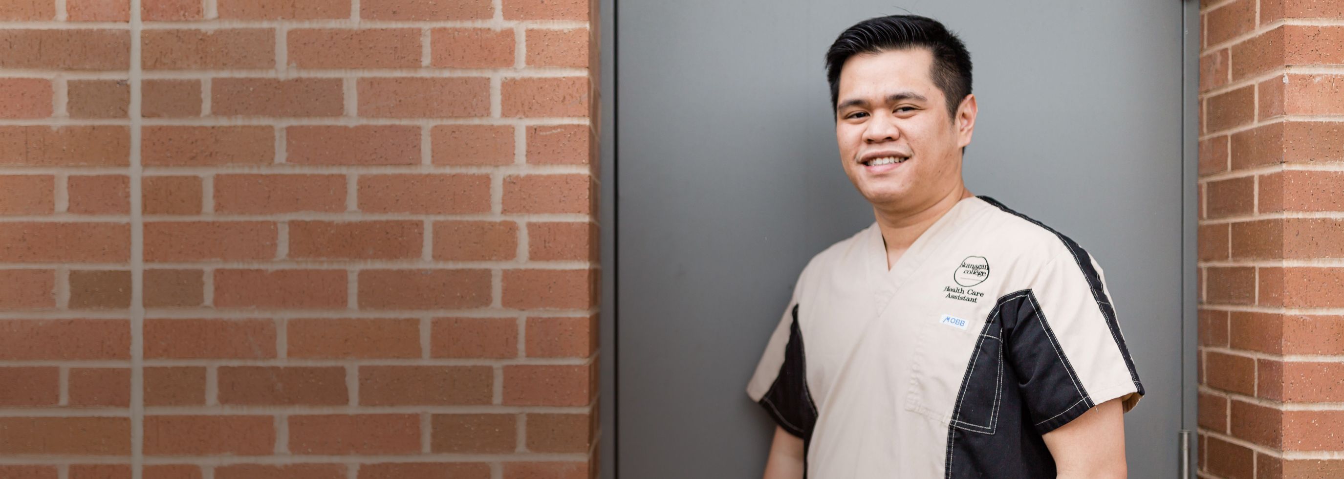 Male health student standing by a brick wall wearing his 91̽ health program uniform shirt